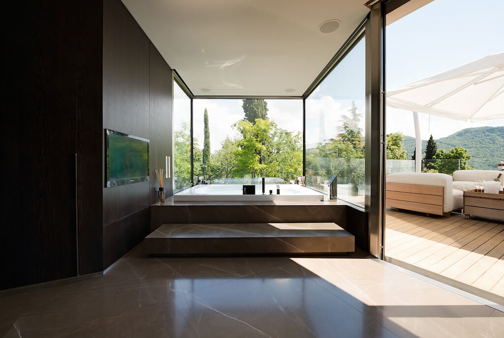 A photo of the master bathroom featuring two walls of security windows in a luxury home, opening to a patio.
