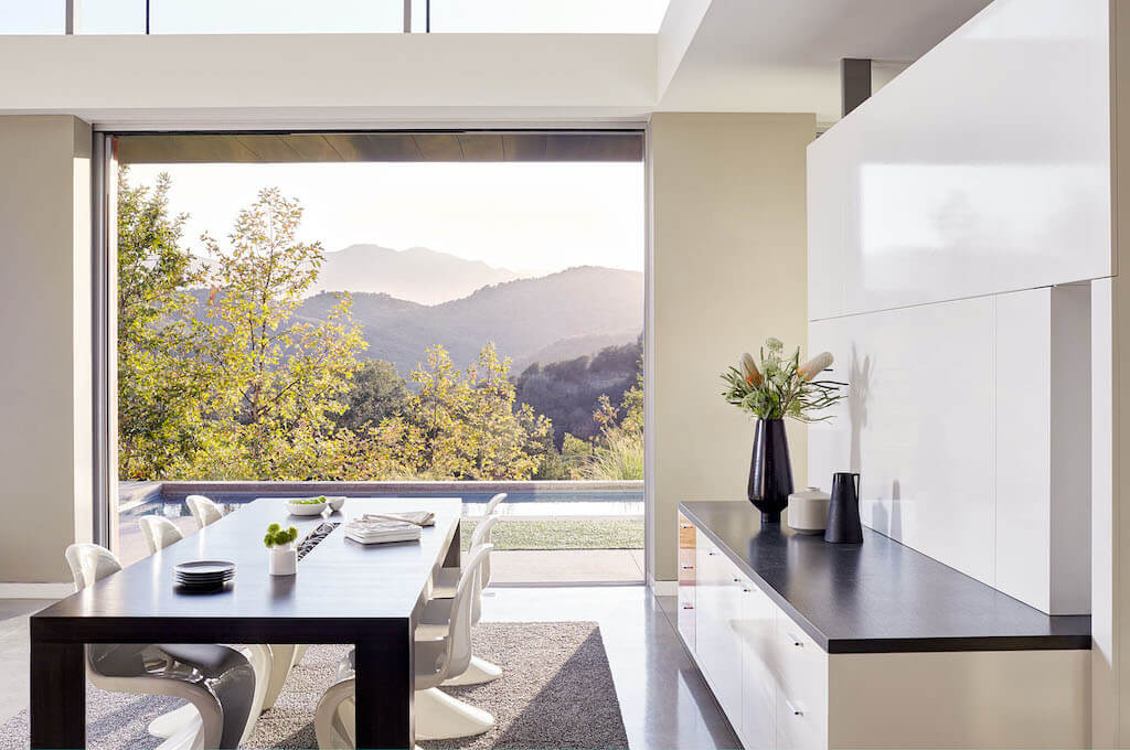 A photo of a luxury home dining room with a large fixed window overlooking mountains.