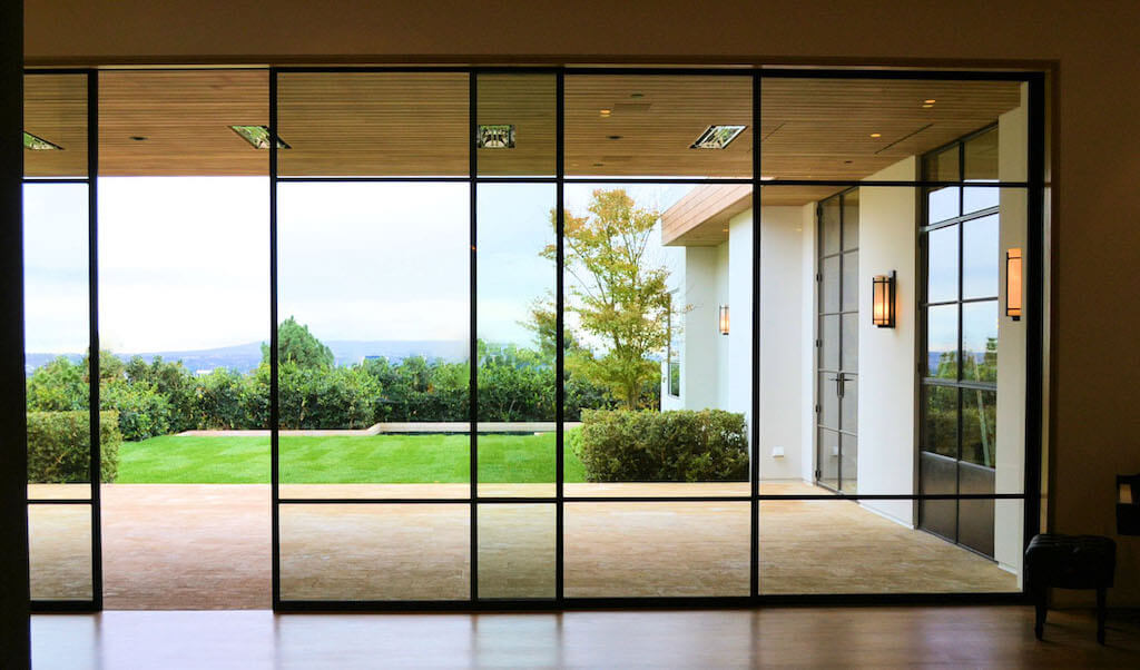 A photo of a security glass window wall opening up to the private backyard of a luxury home.