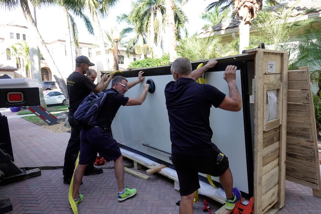 A photo of a team of movers unpacking a custom security door outside a luxury home.